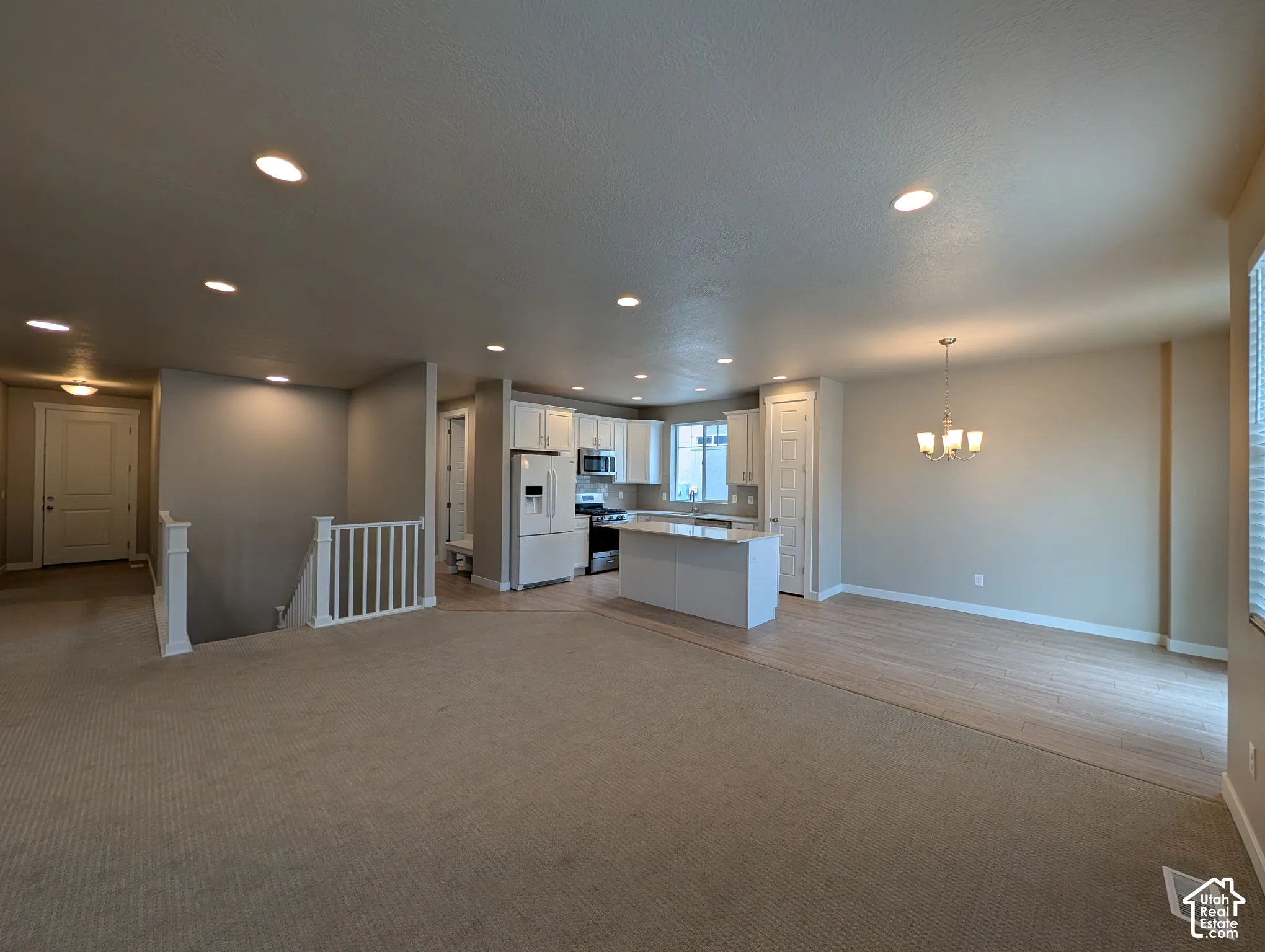 Open-concept interior featuring recessed lighting, white cabinetry, a kitchen island with countertop seating, wood-finish flooring, and a white balustrade staircase