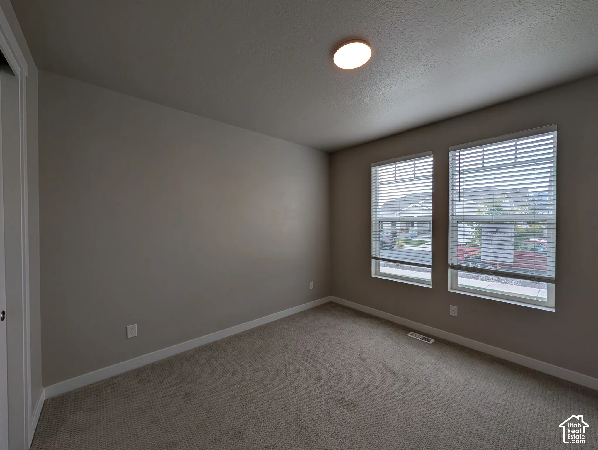 Neutral-toned interior space featuring neutral wall-to-wall carpeting, dual windows with integrated blinds, and a central flush-mount ceiling light fixture