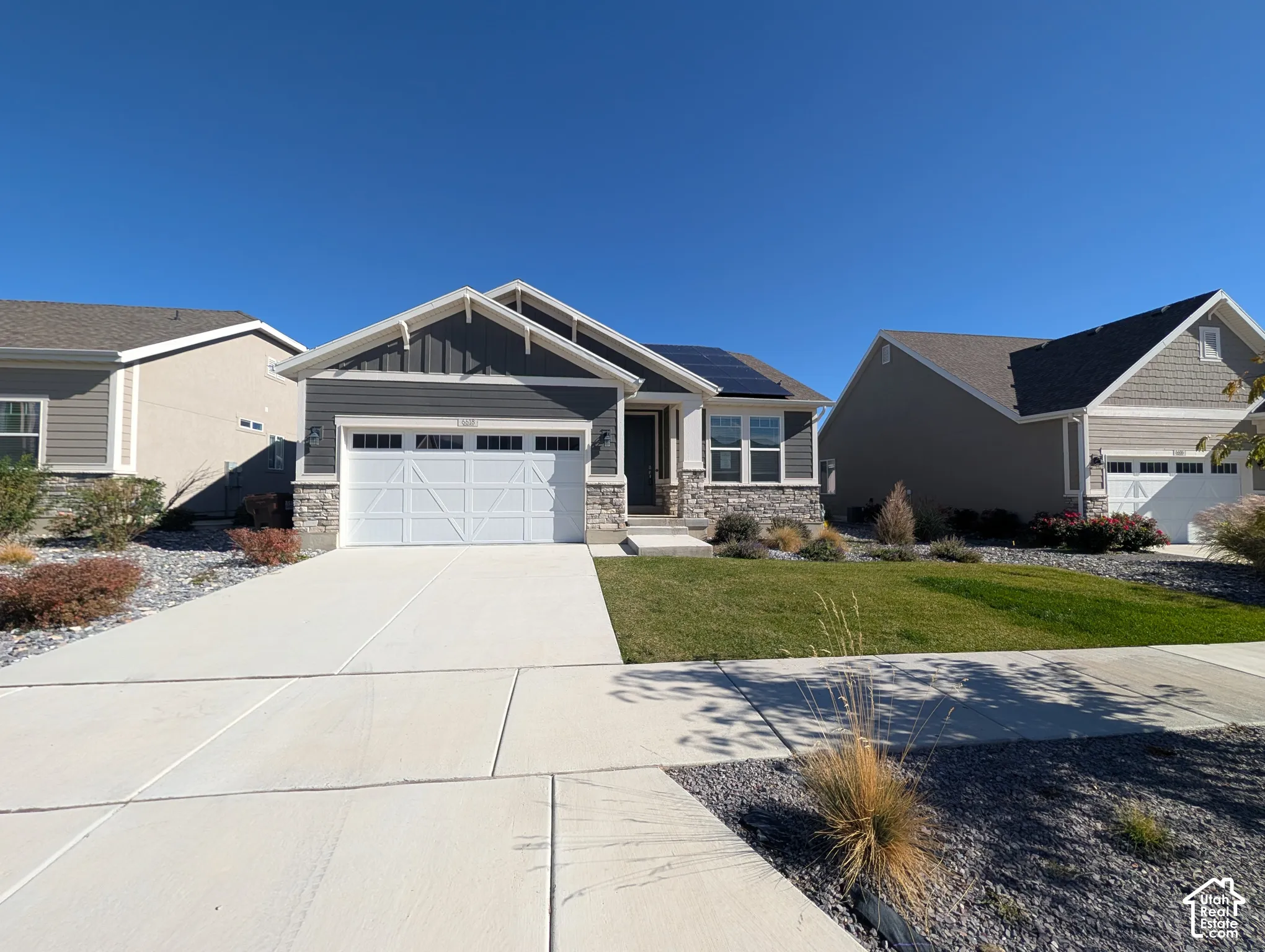 Single-story residence featuring a stone and horizontal siding exterior, attached garage with paneled door, solar panels, and manicured landscaping