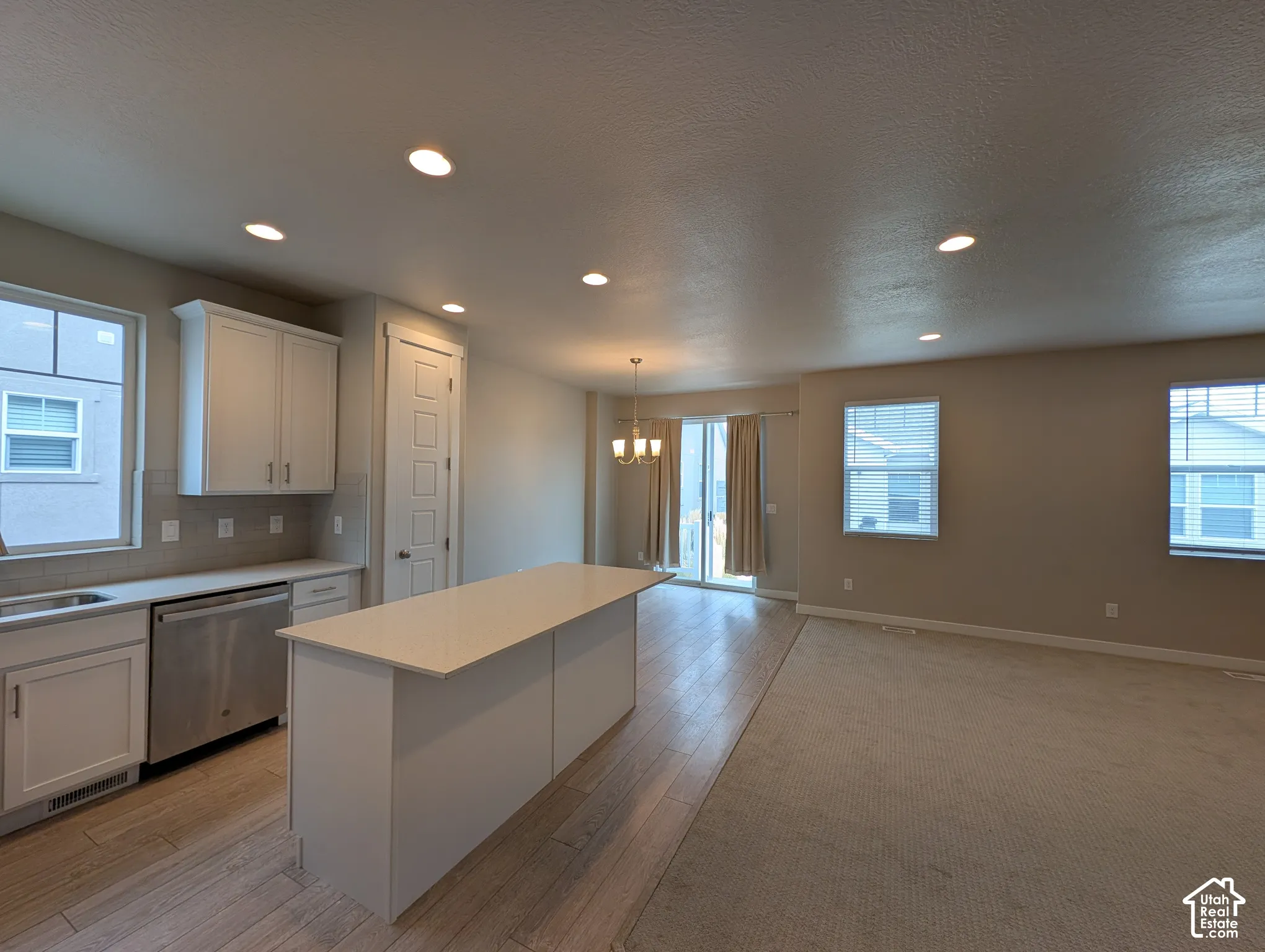 Kitchen featuring white shaker-style cabinetry, an island with stone-finish countertop, stainless steel dishwasher, recessed lighting, and wood-finish flooring