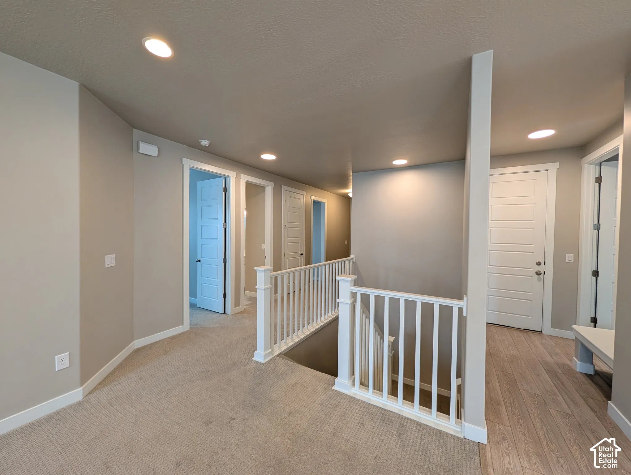 Hallway featuring neutral wall paint, recessed lighting, carpeted flooring, wood-finish flooring, and a white balustrade with a wooden handrail