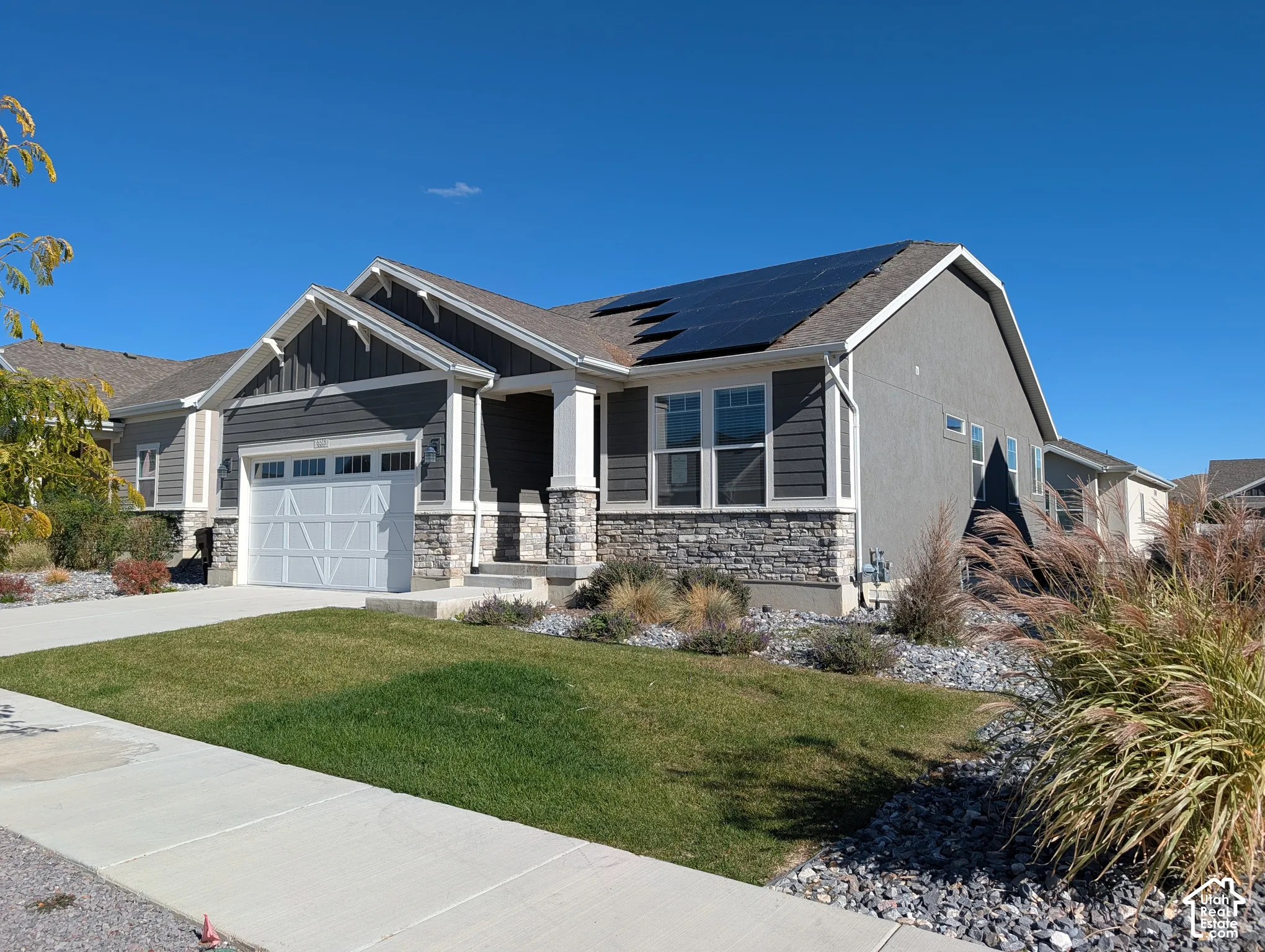 Exterior featuring a stucco and stone veneer facade, roof-mounted solar panels, carriage-style garage door, and low-maintenance xeriscaped landscaping
