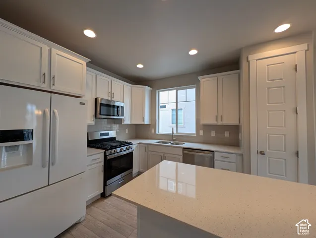 Kitchen featuring white cabinetry, solid-surface countertops, stainless steel appliances, a double-basin undermount sink, and wood-finish flooring