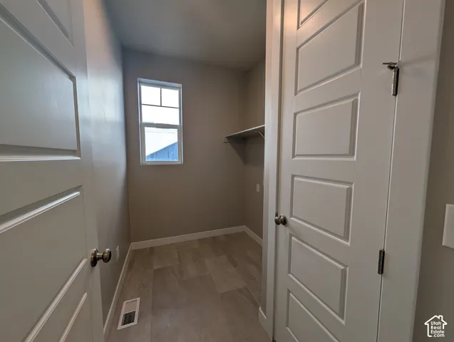 Neutral-toned storage space featuring wood-finish flooring, a single-hung window, and built-in shelving