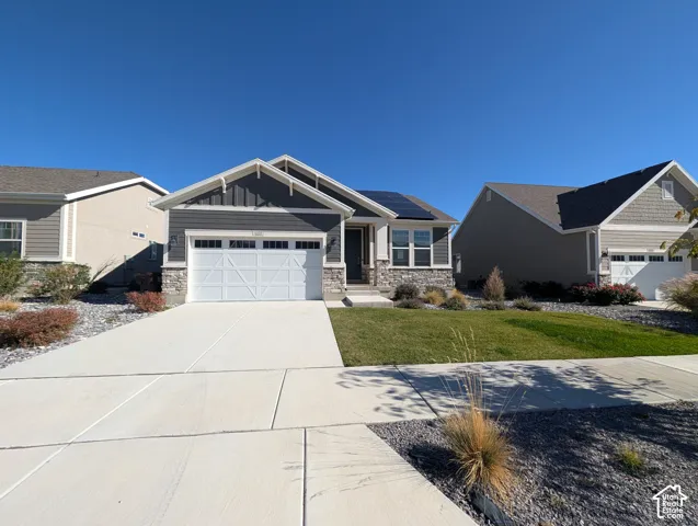 Single-story residence featuring a stone and horizontal siding exterior, attached garage with paneled door, solar panels, and manicured landscaping