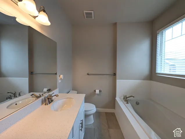 Bathroom featuring a stone-composite countertop with an integrated basin, white cabinetry, a deep soaking tub, polished metal hardware, and wood-finish flooring