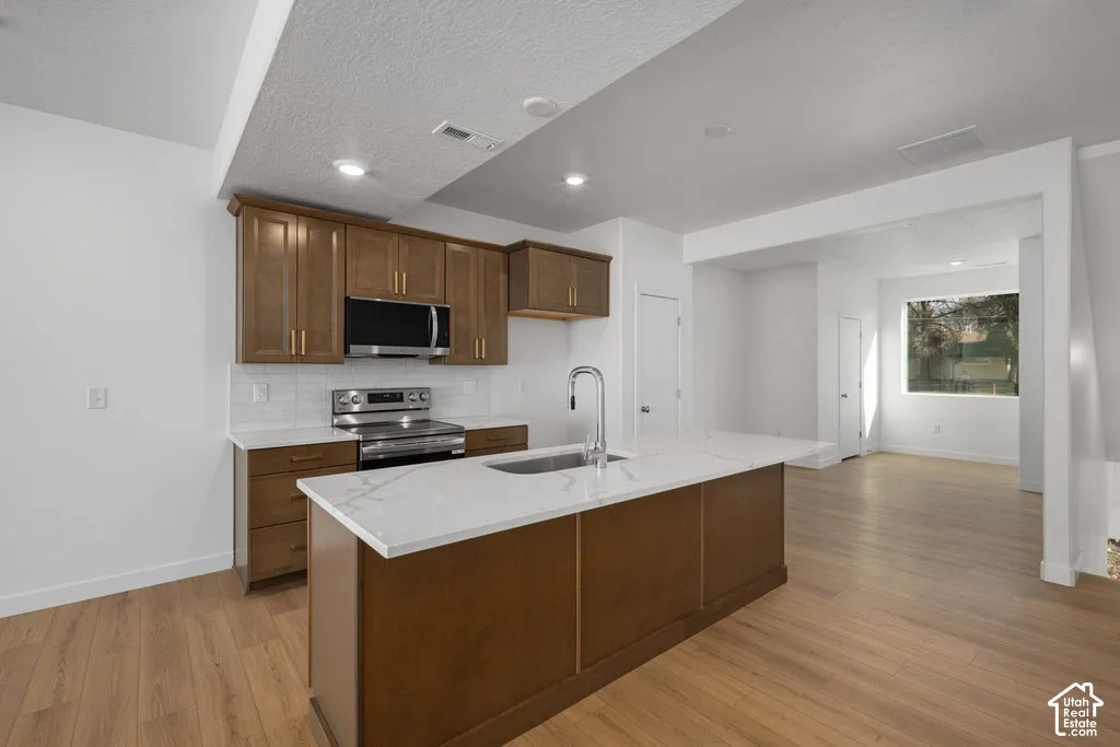Kitchen featuring a central island with a solid-surface countertop, wood-finish cabinetry, built-in stainless steel appliances, and wood-finish flooring