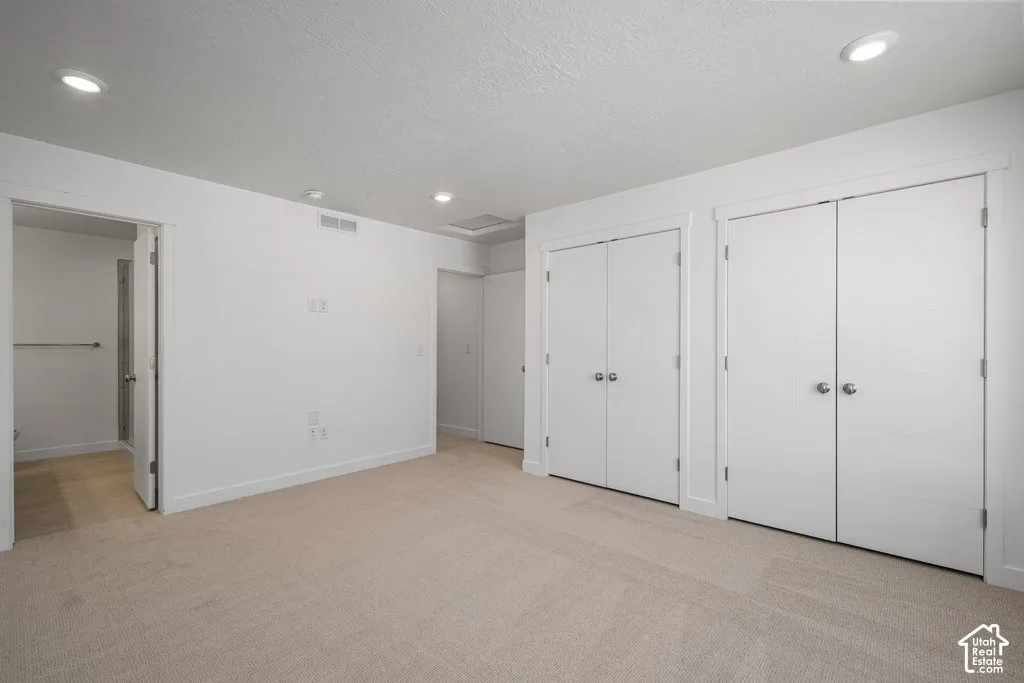 Neutral-toned carpeting, recessed ceiling lighting, and dual sets of double-door closets featuring round metal hardware