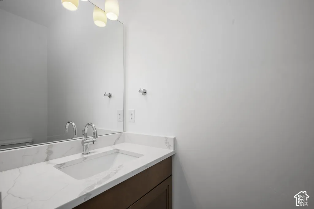 Vanity featuring a stone-patterned countertop with an integrated rectangular basin, wood-finish cabinetry, polished chrome gooseneck faucet, large frameless wall-mounted mirror, and three-globe light fixture