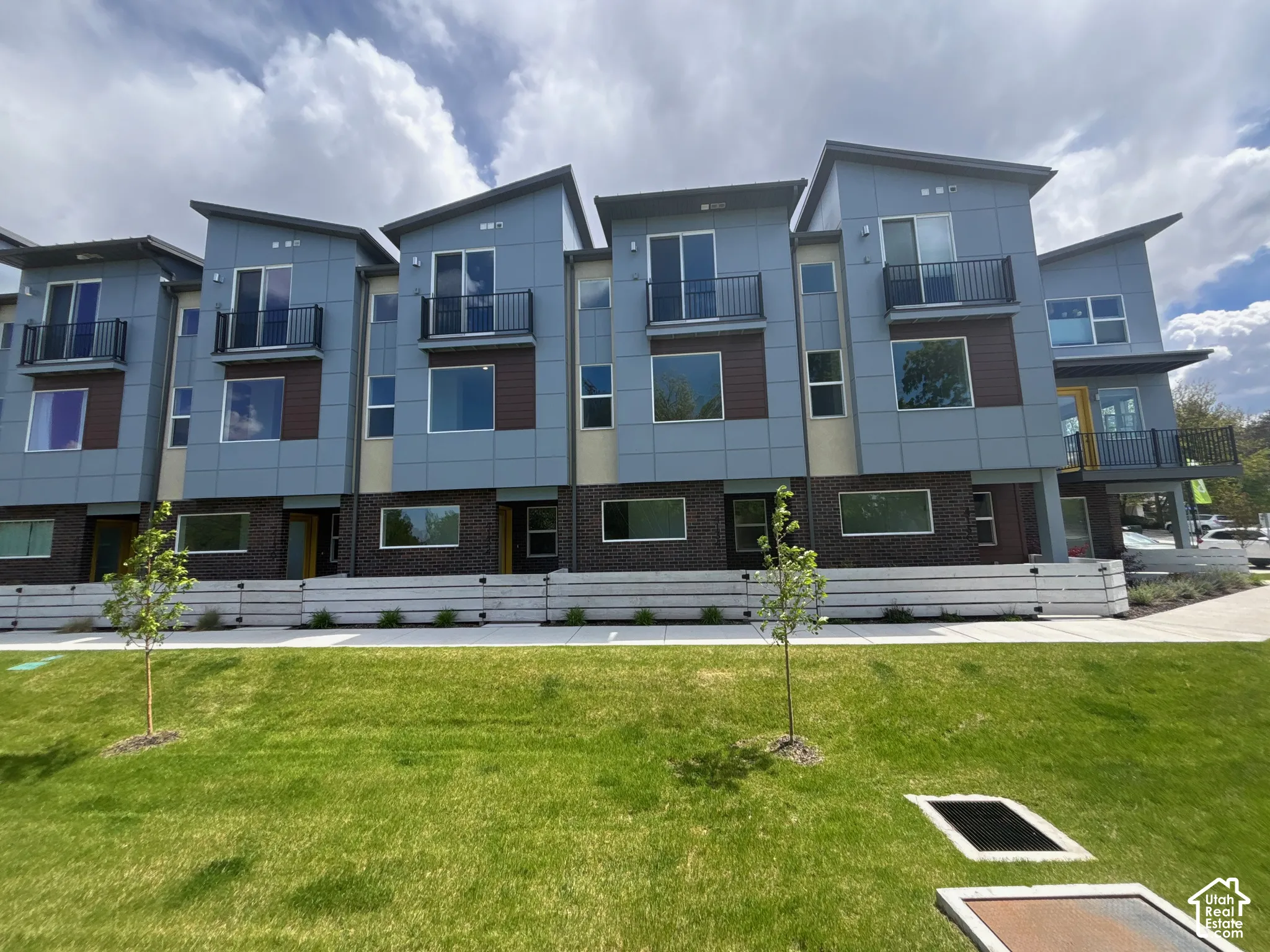 Contemporary multi-level exterior featuring dark brick masonry, blue panel siding, metal balconies, and shed-style rooflines