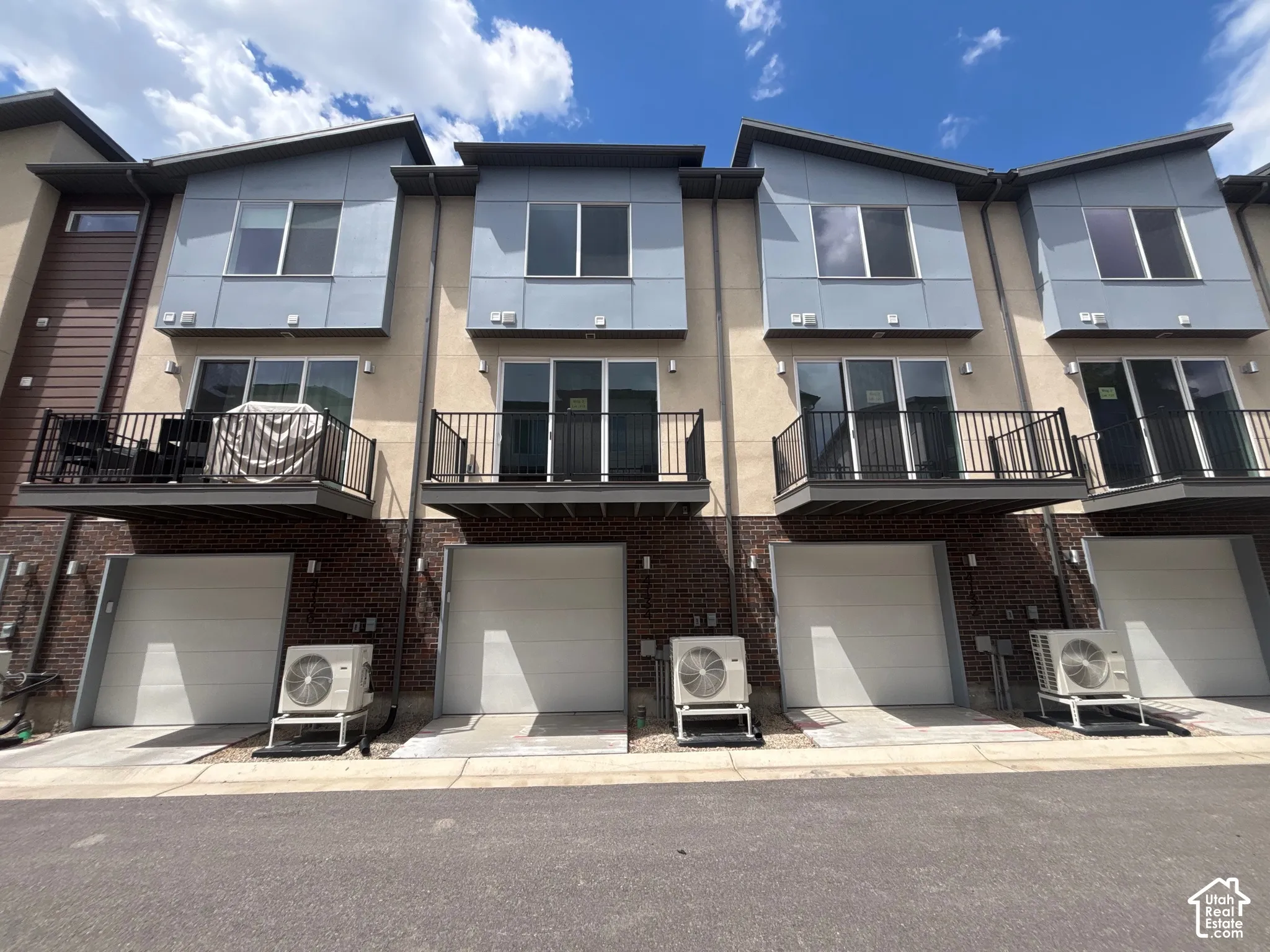 Contemporary multi-level facade featuring a combination of brick, stucco, and panel siding with private balconies, sliding glass doors, and attached single-car garages