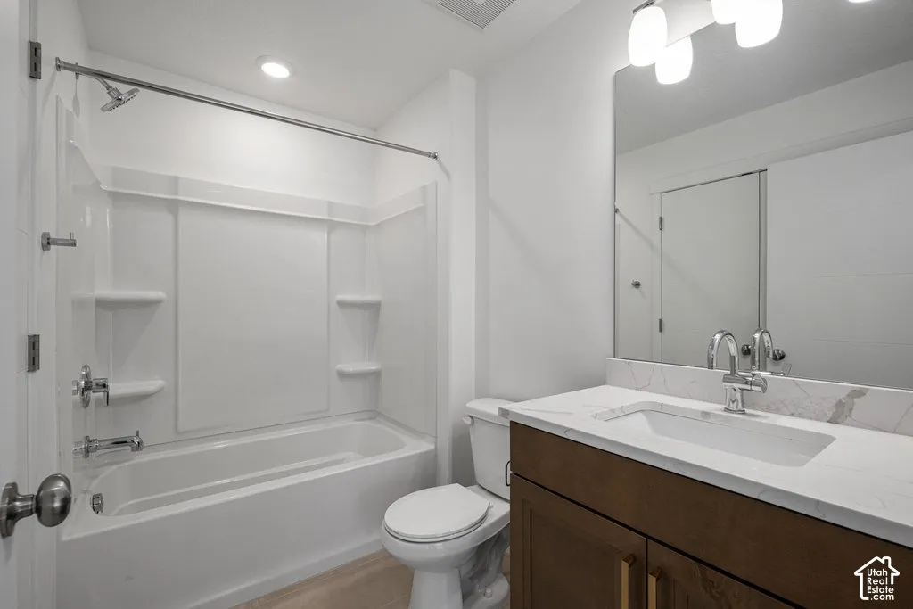 Bathroom featuring a wood-finish vanity with a stone-composite countertop, integrated sink, undermount faucet, and a large-format vanity mirror with integrated lighting