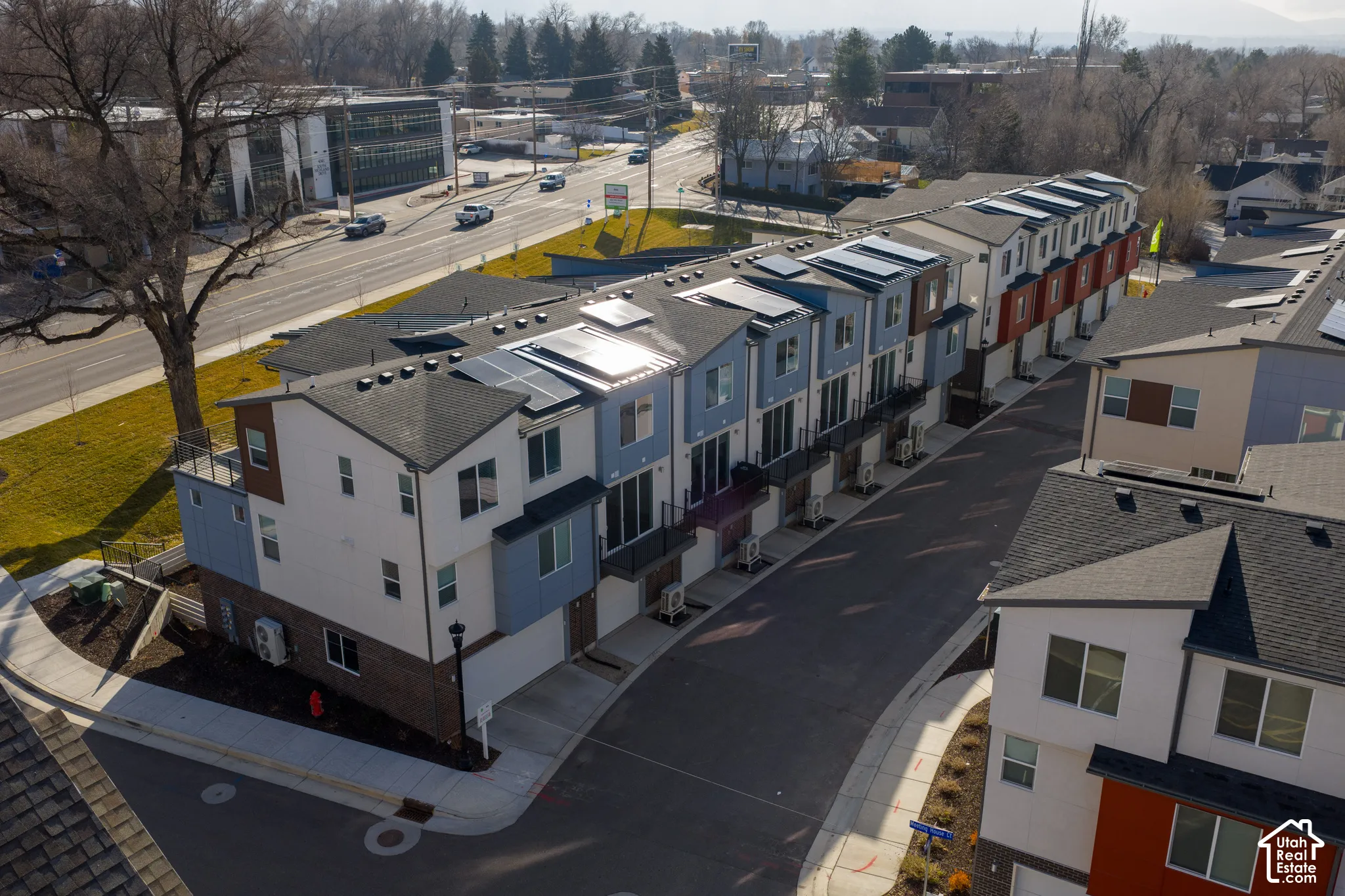 Multi-story townhome complex featuring roof-mounted solar panels, brick and panel siding, private balconies, and asphalt driveways