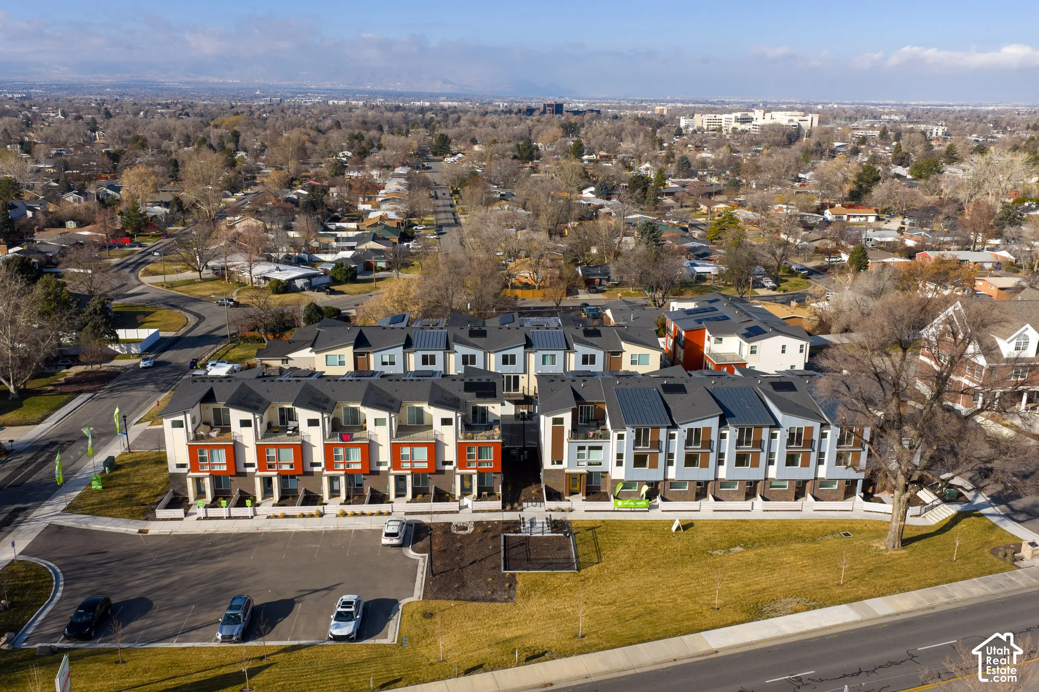 Aerial perspective of a multi-unit residential complex featuring contemporary multi-story architecture, metal roofing, integrated solar panels, private balconies, and dedicated surface parking