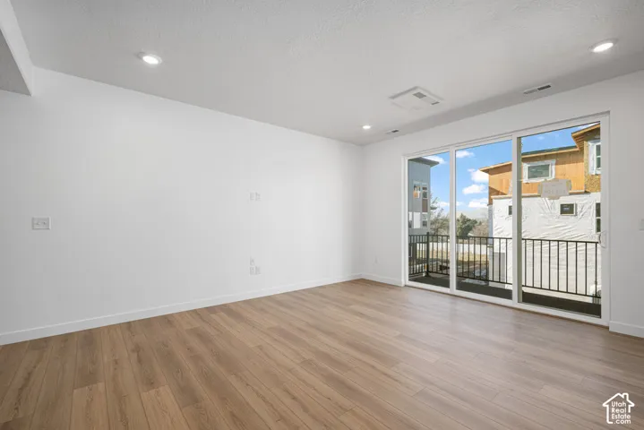 Interior space featuring wood-finish flooring, recessed lighting, and large sliding glass doors opening to a balcony with metal railing