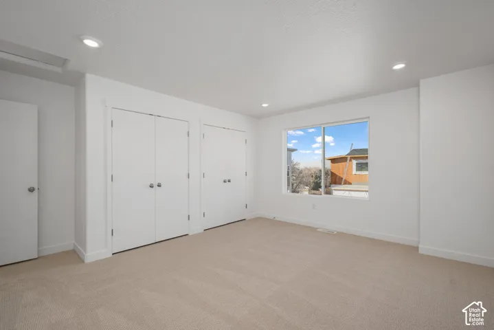 Neutral-toned wall-to-wall carpeting, recessed ceiling lighting, dual-door closets, and a large sliding window