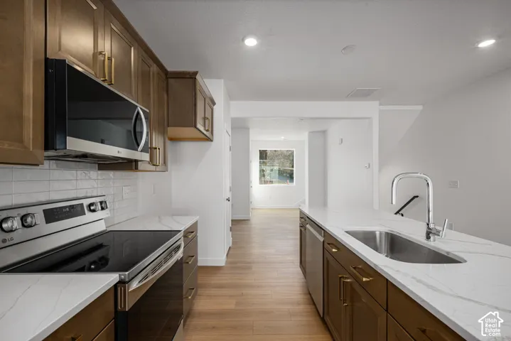 Kitchen featuring wood-finish cabinetry, stone-style countertops, white subway tile backsplash, stainless steel appliances, and a central island with a stainless steel undermount sink