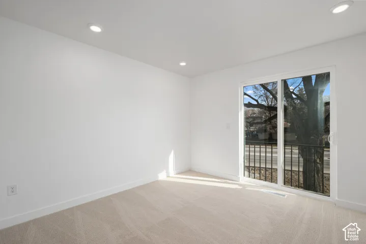 Neutral interior featuring recessed lighting, wall-to-wall carpeting, and a sliding glass door with an integrated black metal railing