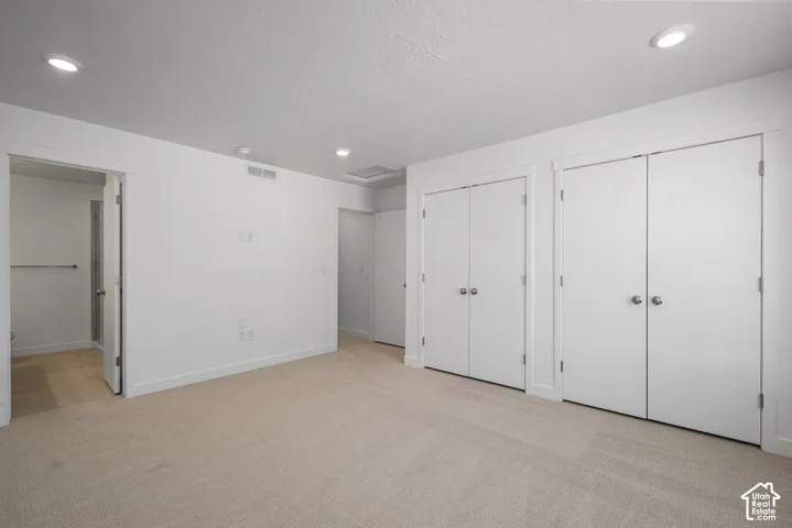 Neutral-toned carpeting, recessed ceiling lighting, and dual sets of double-door closets featuring round metal hardware