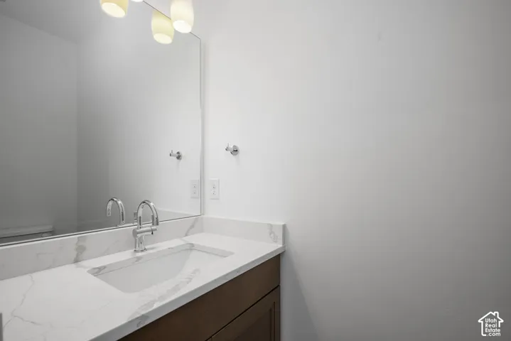 Vanity featuring a stone-patterned countertop with an integrated rectangular basin, wood-finish cabinetry, polished chrome gooseneck faucet, large frameless wall-mounted mirror, and three-globe light fixture
