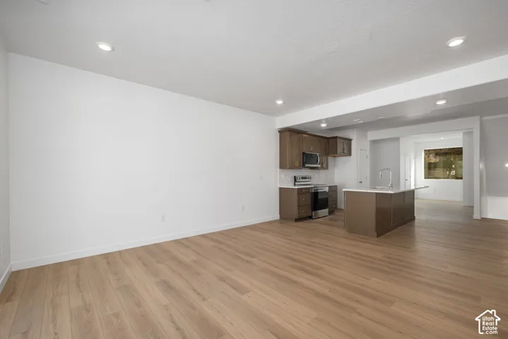 Open-concept space featuring wood-finish flooring, recessed lighting, stained-wood cabinetry, stainless steel appliances, and a central kitchen island