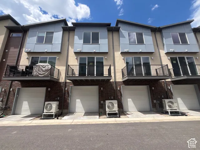 Contemporary multi-level facade featuring a combination of brick, stucco, and panel siding with private balconies, sliding glass doors, and attached single-car garages