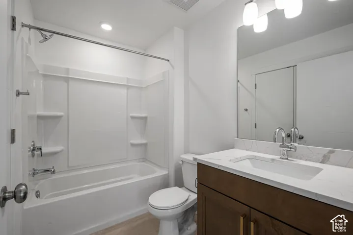 Bathroom featuring a wood-finish vanity with a stone-composite countertop, integrated sink, undermount faucet, and a large-format vanity mirror with integrated lighting