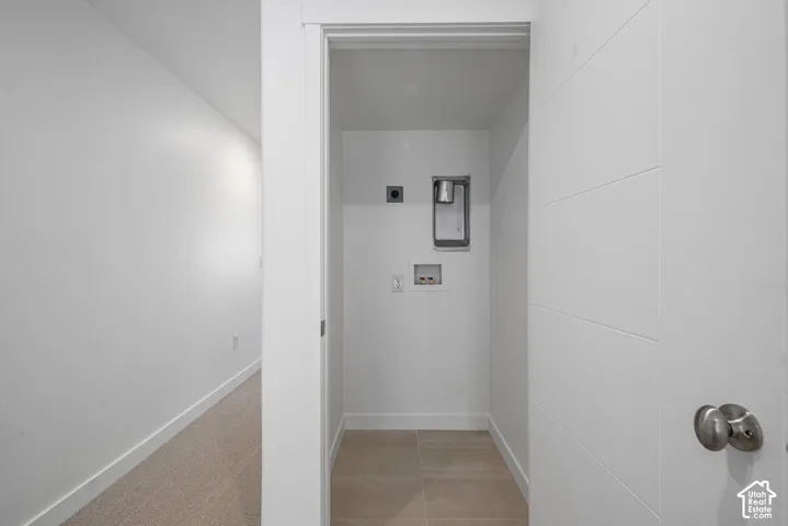 Utility closet featuring neutral tile flooring, laundry hookups, and a white paneled door with brushed nickel hardware