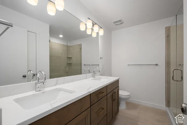 Double vanity with stone-look countertops, undermount sinks, wood-finish cabinetry, full-width mirror, and a glass-enclosed shower with tile surround