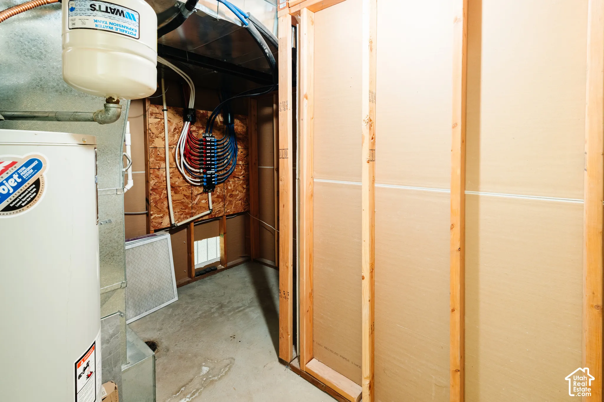Utility area featuring an expansion tank, water heater, exposed wood-frame wall construction, and a water distribution manifold system