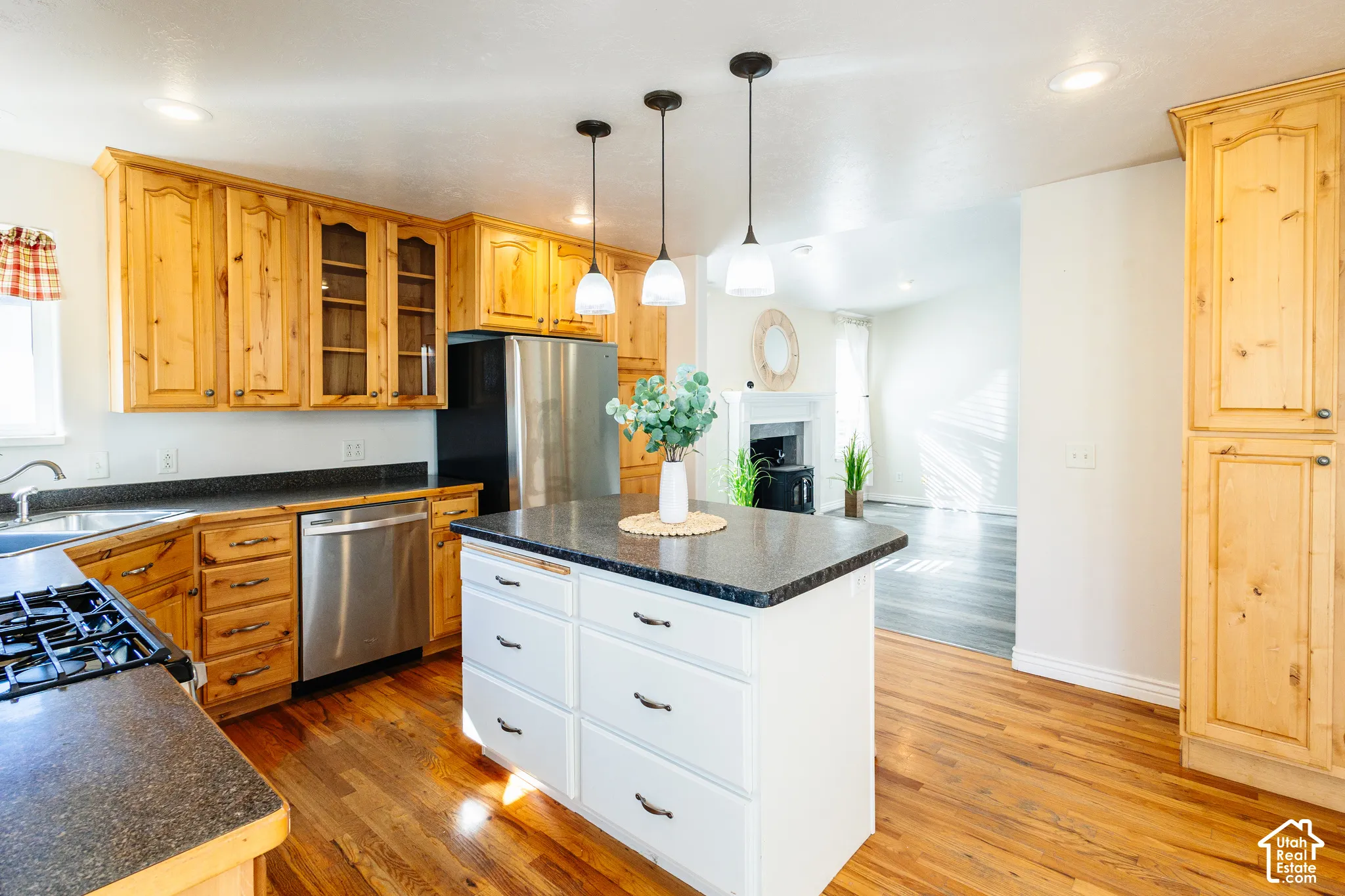 Kitchen featuring natural wood cabinetry, central island with storage drawers, stainless steel appliances, dark stone-finish countertops, and trio of pendant light fixtures