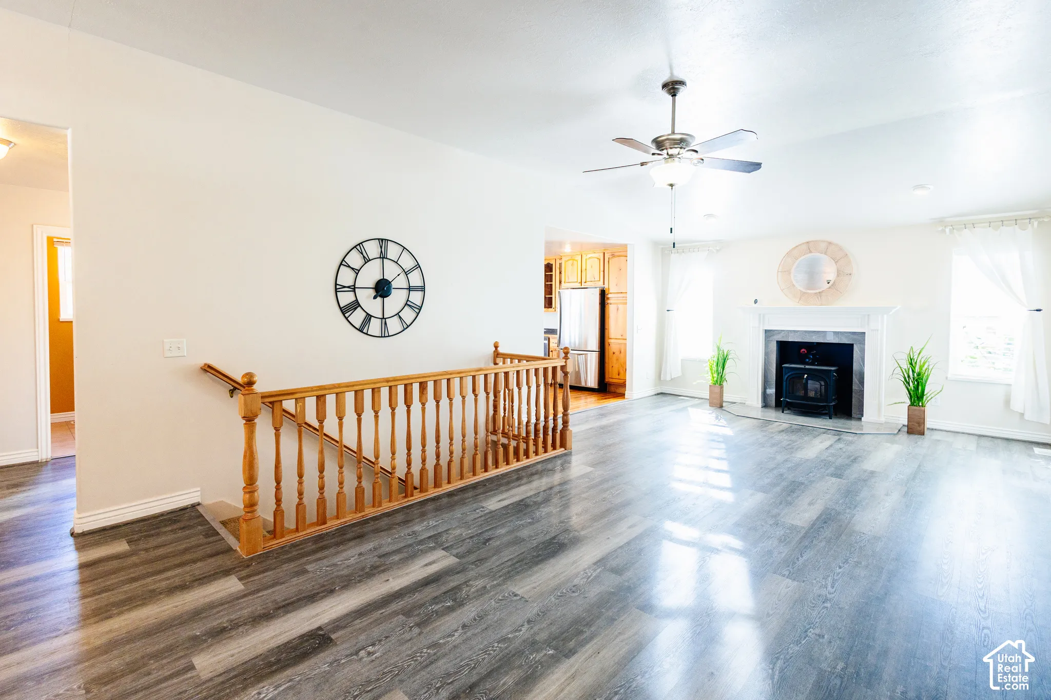 Open living area featuring wood-finish flooring, a fireplace with a mantel, a ceiling fan, and a wood balustrade staircase