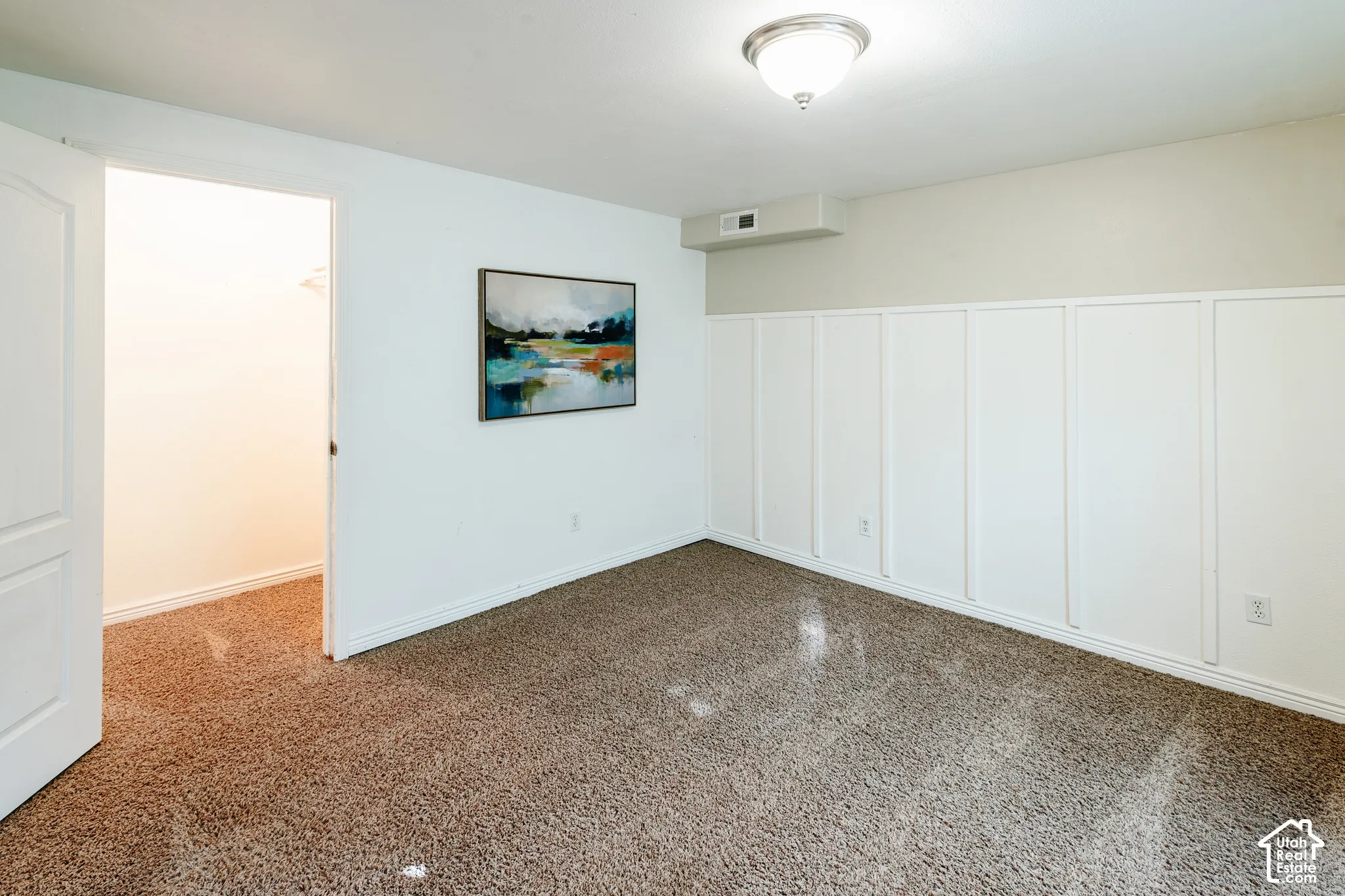 Interior space featuring wall-to-wall carpeting, white board-and-batten wainscoting, a flush-mount ceiling light fixture, and an integrated walk-in closet