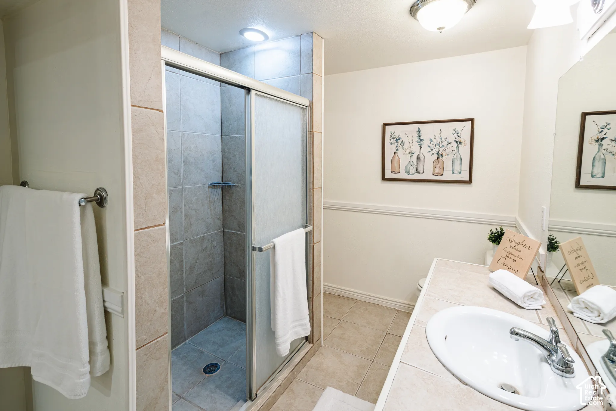 Bathroom featuring a tile-surround shower with a sliding glass door, a tile-topped vanity with an integrated basin, a large wall-mounted mirror, and tile flooring