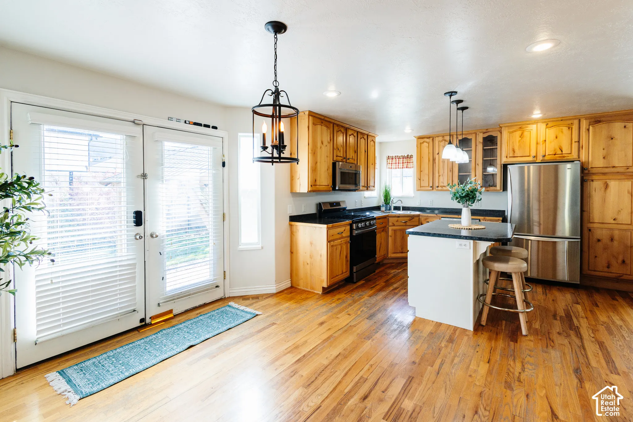 Kitchen featuring wood-finish flooring, natural wood cabinetry, dark solid-surface countertops, stainless steel appliances, and a central island with built-in cabinetry