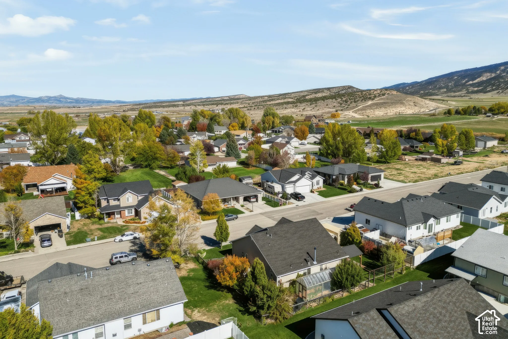 Aerial perspective of a suburban neighborhood featuring paved streets, mature deciduous trees, residential dwellings with pitched roofing, and an expansive mountain range backdrop