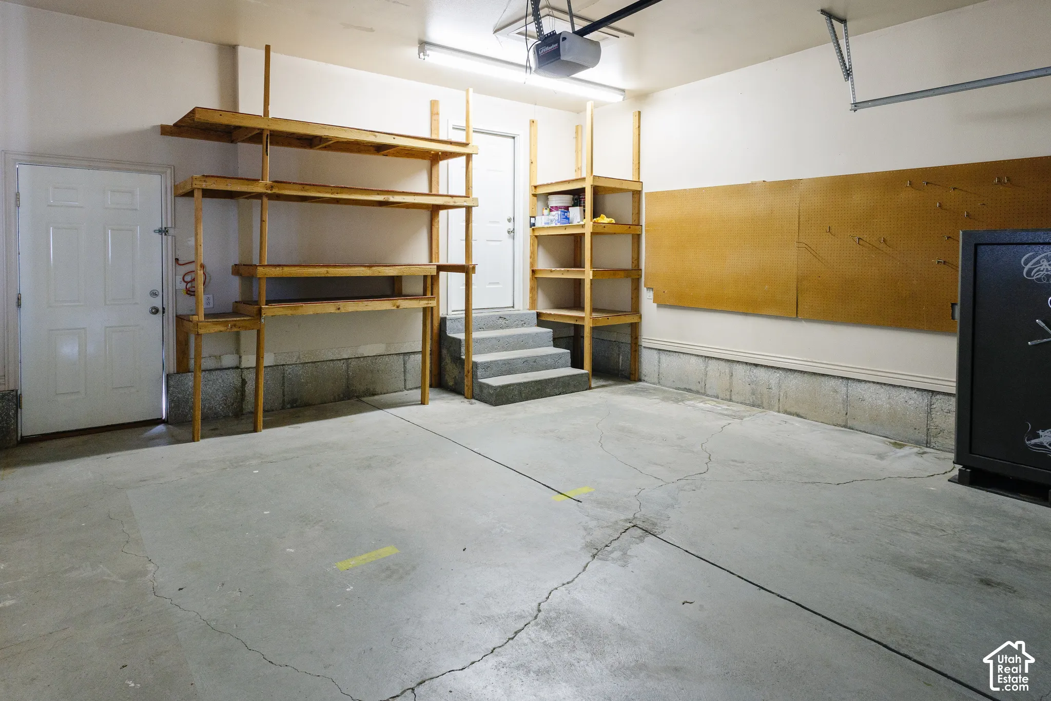 Garage space featuring built-in wooden shelving units, concrete flooring, fluorescent overhead lighting, and a wall-mounted corkboard panel