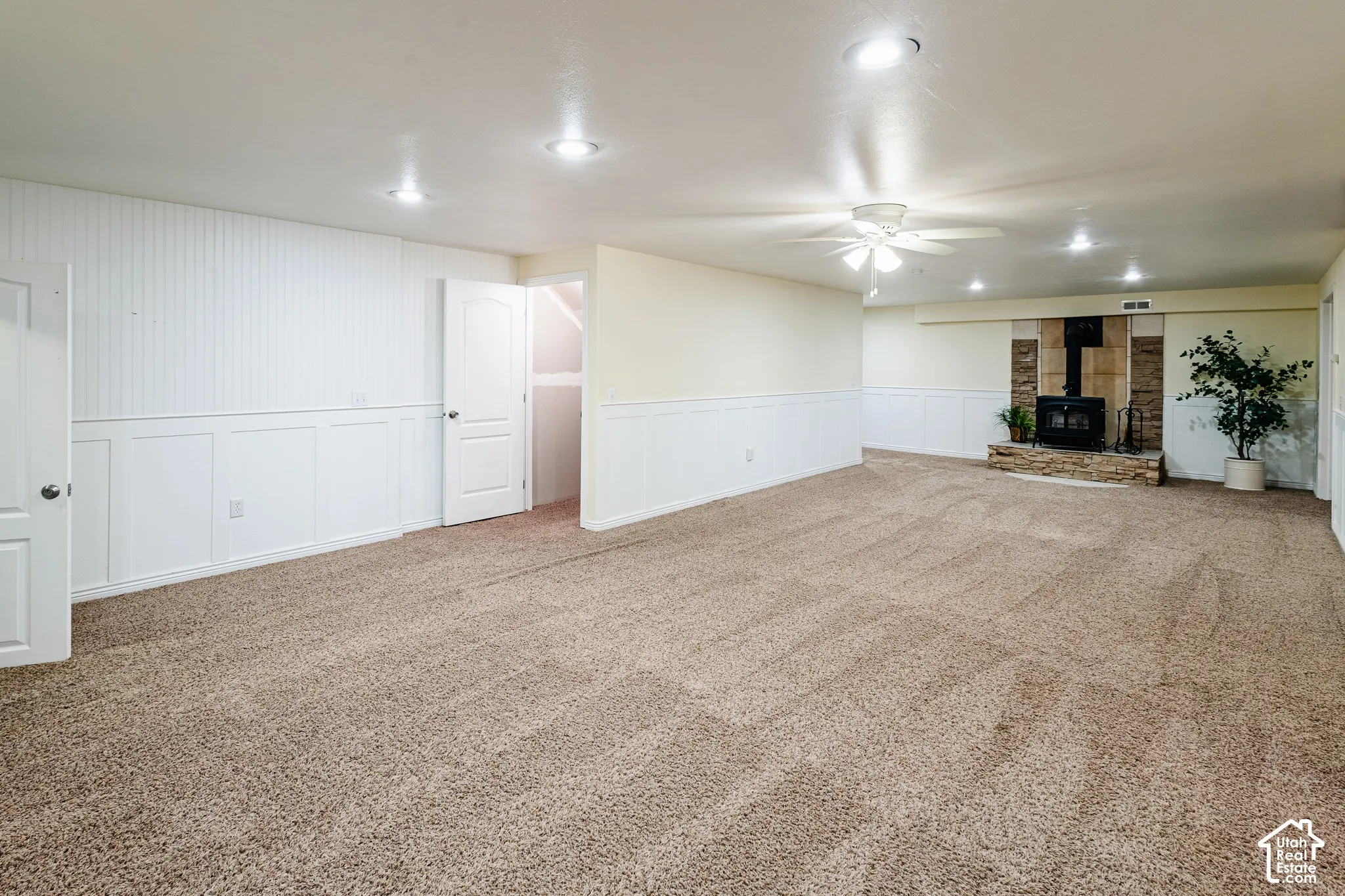 Spacious room featuring wall-to-wall carpeting, wood-paneled wainscoting, recessed ceiling lighting, a ceiling fan, and a floor-to-ceiling stone fireplace surround