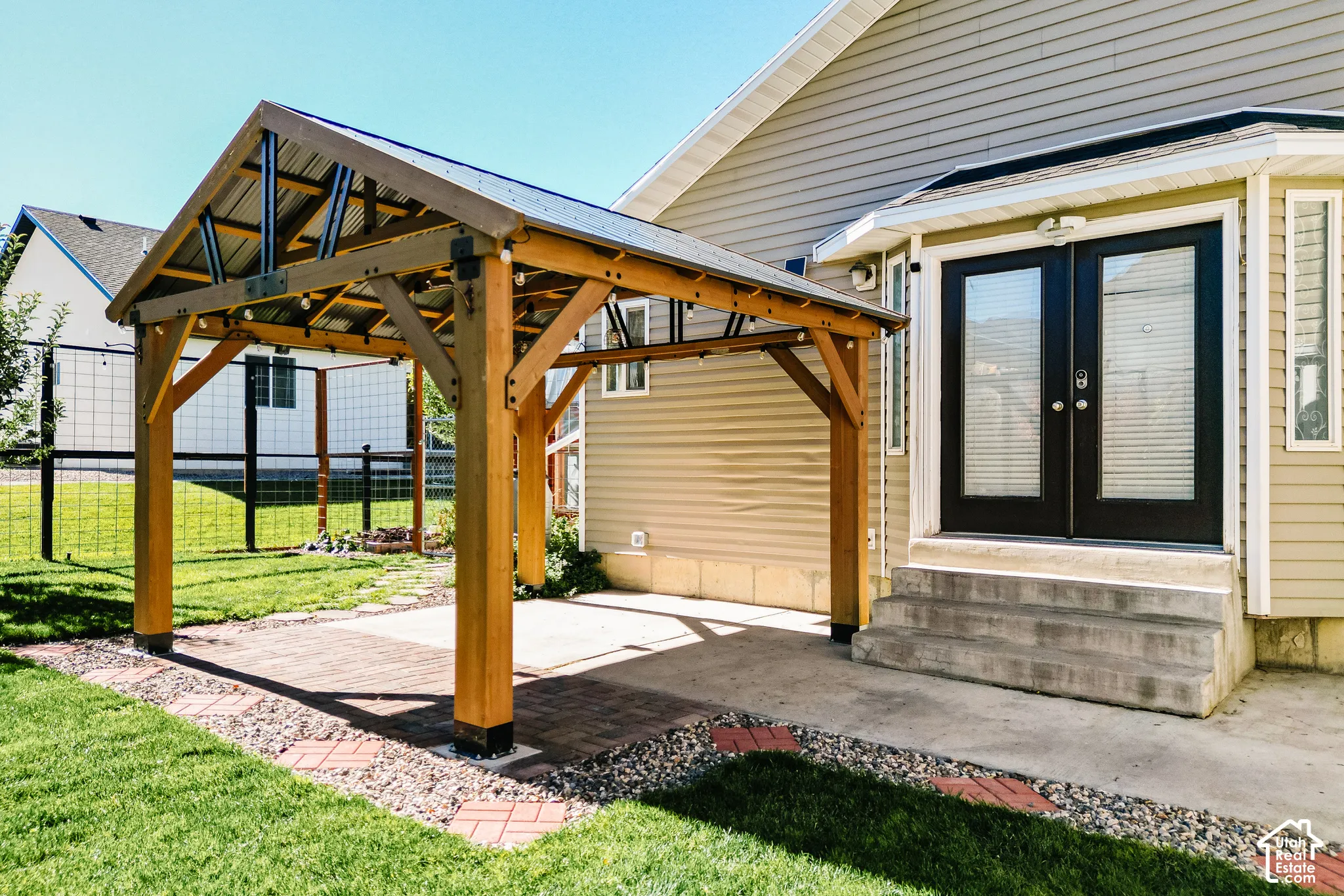Custom timber-frame gazebo with a metal roof, concrete patio, brick paver accents, and double-glass pane French doors