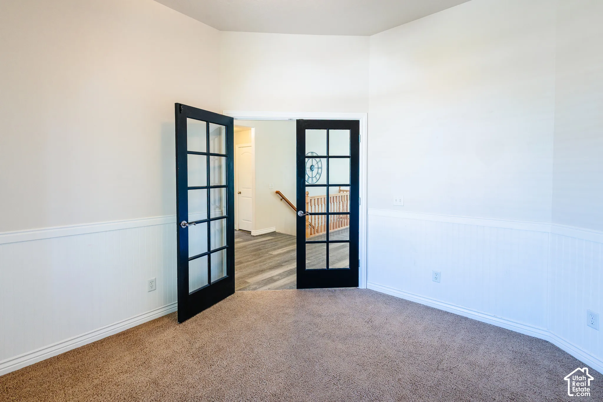 Interior room featuring black-framed French doors, white beadboard wainscoting, and neutral wall-to-wall carpeting