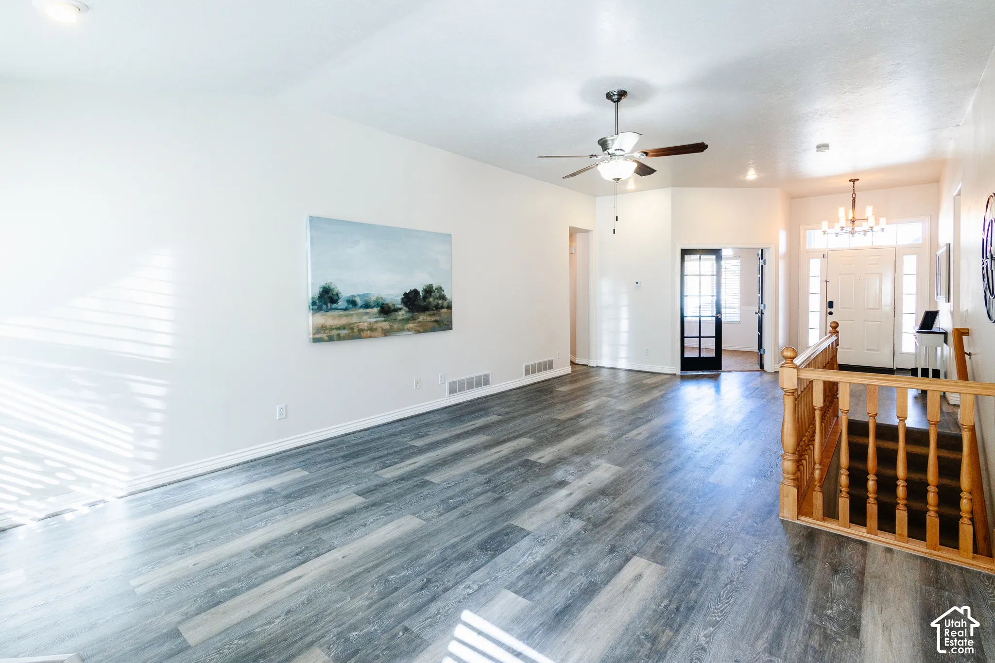 Wood-finish flooring, vaulted ceilings, a ceiling fan with integrated lighting, a multi-pane glass door, and wooden staircase railing