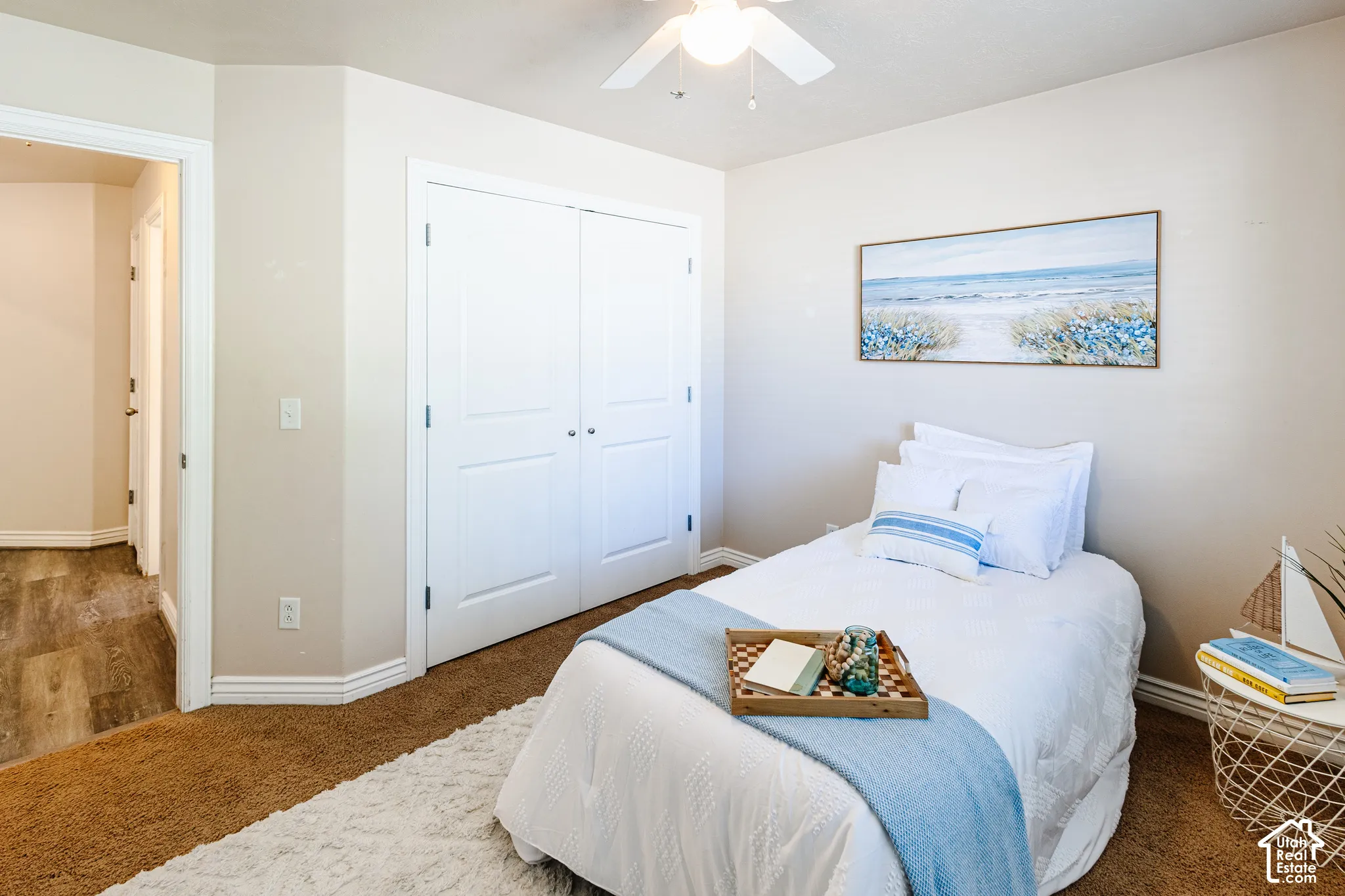 Neutral-toned interior featuring dual-panel closet doors, textured wall-to-wall carpeting, and an attached ceiling fan with integrated lighting