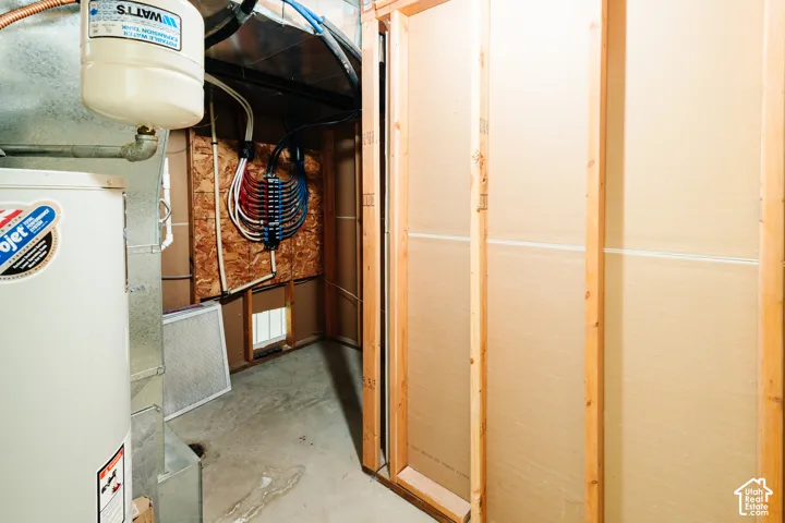 Utility area featuring an expansion tank, water heater, exposed wood-frame wall construction, and a water distribution manifold system