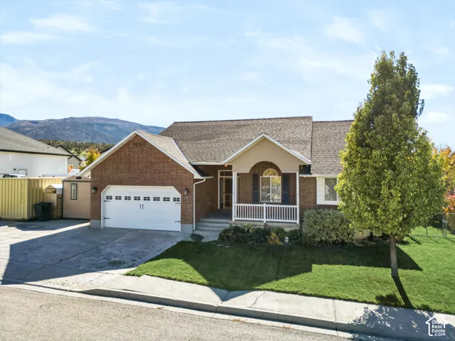 Single-story residence featuring a brick facade, covered front porch with white railing, asphalt shingle roof, multi-car garage, and concrete driveway