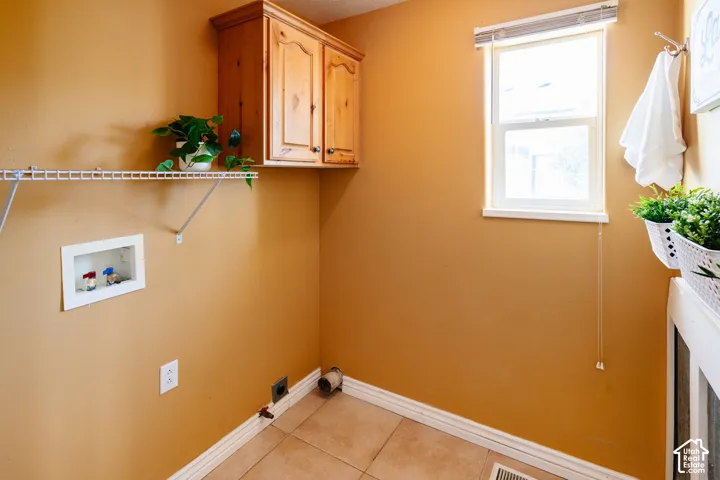 Laundry room featuring tile flooring, wood cabinetry, a built-in wire shelving unit, and a window with a roller shade