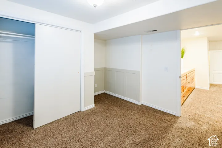 Interior space featuring wall-to-wall carpeting, recessed panel wainscoting, a sliding door closet, and an integrated ceiling light fixture