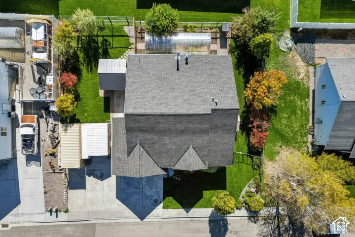 Aerial perspective featuring a multi-gabled asphalt shingle roof, concrete driveway, attached carport, enclosed greenhouse, and landscaped lawn with mature trees