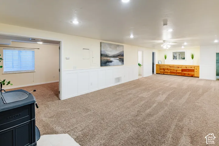 Spacious interior featuring recessed lighting, wall-mounted board and batten wainscoting, carpeted flooring, and a black cast-iron wood-burning stove on a hearth