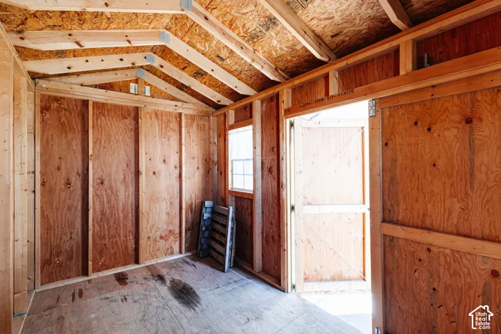 Interior of an outbuilding featuring unfinished wood-paneled walls, exposed timber roof framing, wood-panel flooring, and a window