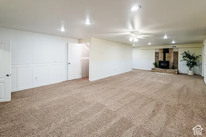 Spacious room featuring wall-to-wall carpeting, wood-paneled wainscoting, recessed ceiling lighting, a ceiling fan, and a floor-to-ceiling stone fireplace surround